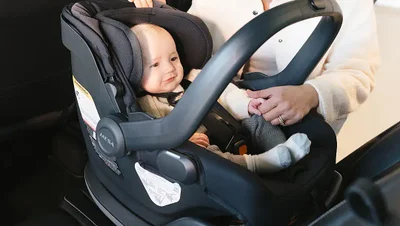 Mother putting a baby in car seat into car