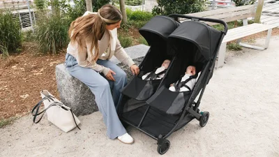 Parent beside the UPPAbaby Minu Duo stroller outdoors with two children seated inside
